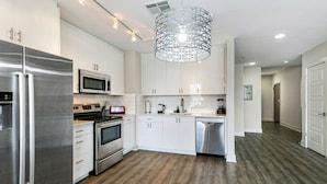 A modern kitchen with stainless steel appliances, white cabinetry, and a unique geometric pendant light. - Spacious Condo in California Building (New Orleans)