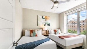 A hotel room with two beds, a ceiling fan, a large window with a city view, and a painting on the wall. - Spacious Condo in California Building (New Orleans)