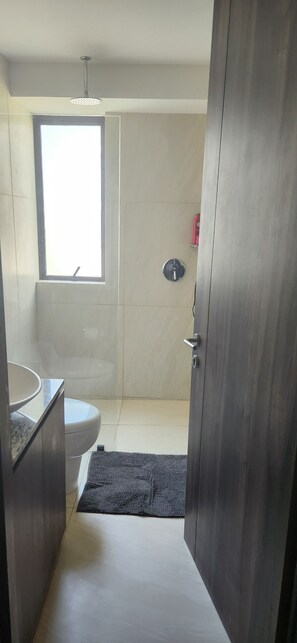 A modern bathroom with a toilet, a sink, a shower, and a window.