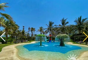 A pool area with palm trees, a water slide, and a covered seating area.