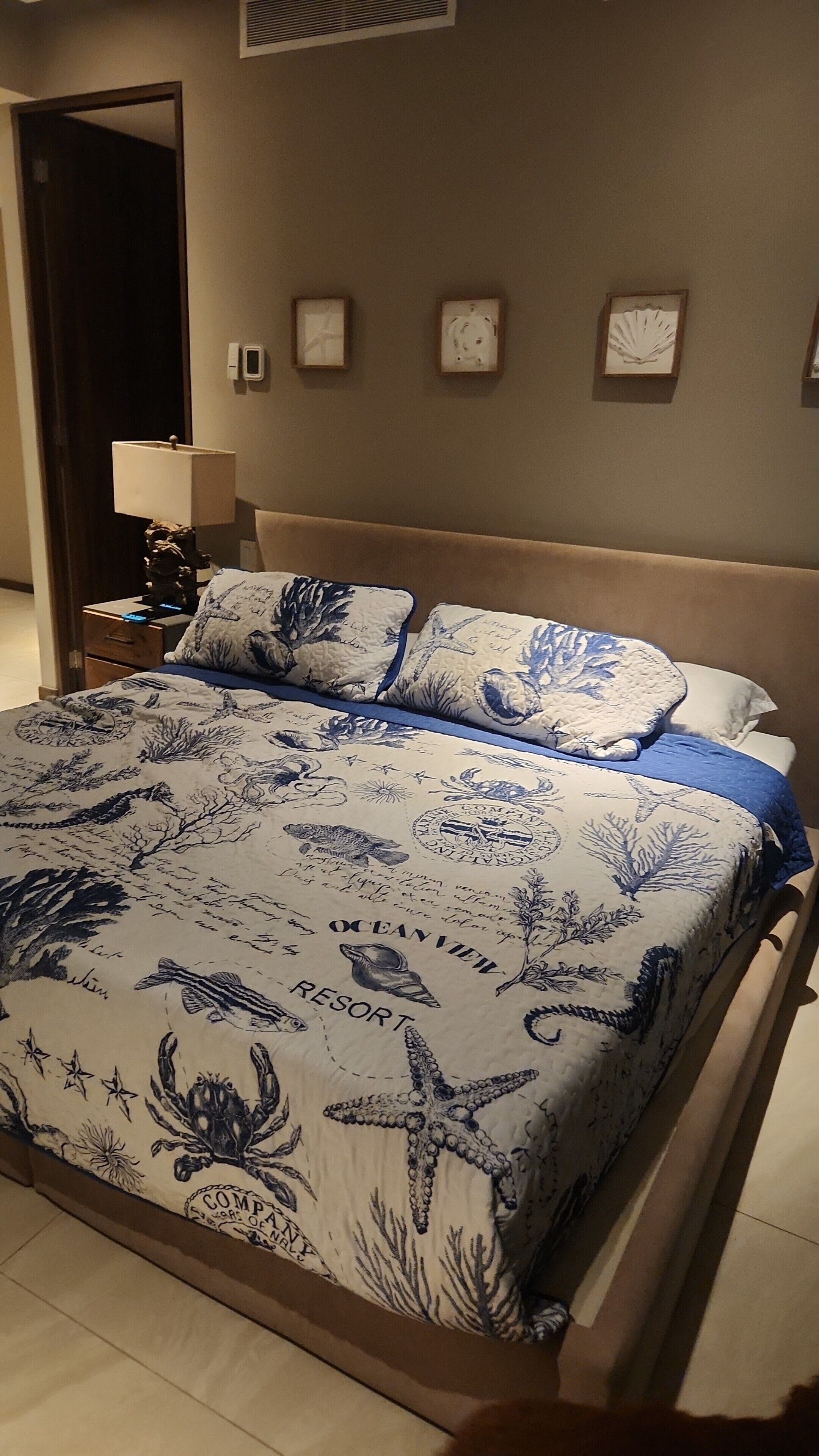 Un lit avec une couvre-lit à motifs nautiques, une t ête de lit en bois et une table de chevet avec une lampe.