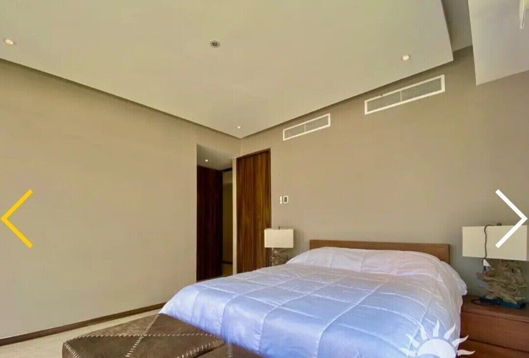 A modern hotel room with a large bed, a wooden headboard, and a nightstand with a lamp.
