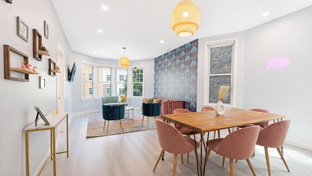 Un comedor moderno con una mesa de madera y sillas rosadas, un sofá azul y una pared con estampado.