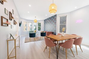 Un comedor moderno con una mesa de madera y sillas rosadas, un sofá azul y una pared con estampado.
