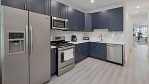 Una cocina moderna con armarios azul oscuro, electrodomésticos de acero inoxidable y un salpicadero de mármol.