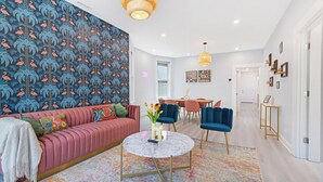 Una sala de estar moderna con pared estampada, un sofá rosa, una mesa de centro redonda y sillas azules.