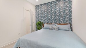 Un dormitorio con cama, pared decorada, puerta y planta.