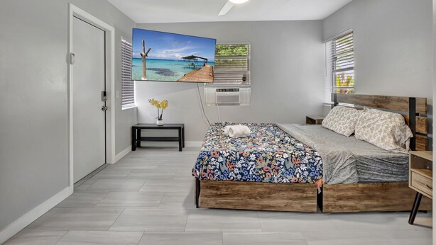 Slaapkamer met een bed, een plafondventilator, een schilderij van een strand en een raam met zonwering.