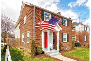 Home at 2810 features a charming red door and a welcoming white porch with an American flag.