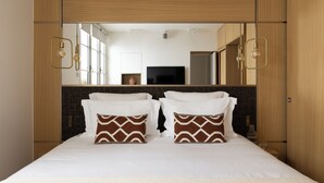 Une chambre d’hôtel avec un grand lit, deux coussins décoratifs, un téléviseur à écran plat et un miroir au-dessus du lit.