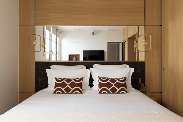 Habitación de hotel con una cama grande, dos almohadones decorativos, un televisor de pantalla plana y un espejo sobre la cama.