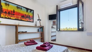 Une pièce comprenant un lit, un tableau, une étagère remplie de livres, une fenêtre donnant sur un paysage agréable et un téléviseur fixé au mur.