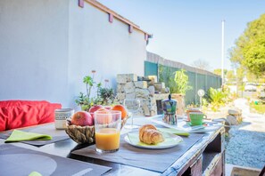 A breakfast table with a croissant, fruit, and juice, set outdoors with a red couch and a stone wall in the background. - Rustico D'aMare - Two Bedroom House, Sleeps 5 (Quartu Santa Elena)