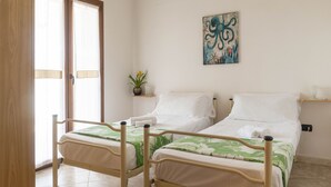 A room with two single beds, a potted plant, a painting, and a sliding glass door.