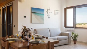 A dining area with a table set for four, a sofa, and a window with a view of the sea.