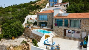 Ein modernes, zweistöckiges Haus mit Naturstein-Fassade, großen Fenstern und einem Swimmingpool.