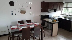 A dining area with a table set for four, a kitchen with dark cabinets, and a window providing natural light.