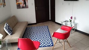 A living room with a sofa, a red chair, a patterned rug, a TV, and a door.