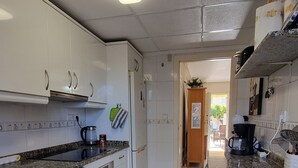Een keuken met witte kastjes, een fornuis, een spoelbak en een vuilnisbak.