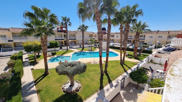 A resort with a central swimming pool, palm trees, and a well-maintained lawn.