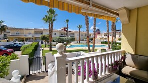 A balcony with a view of a swimming pool, palm trees, and a row of residential buildings.
