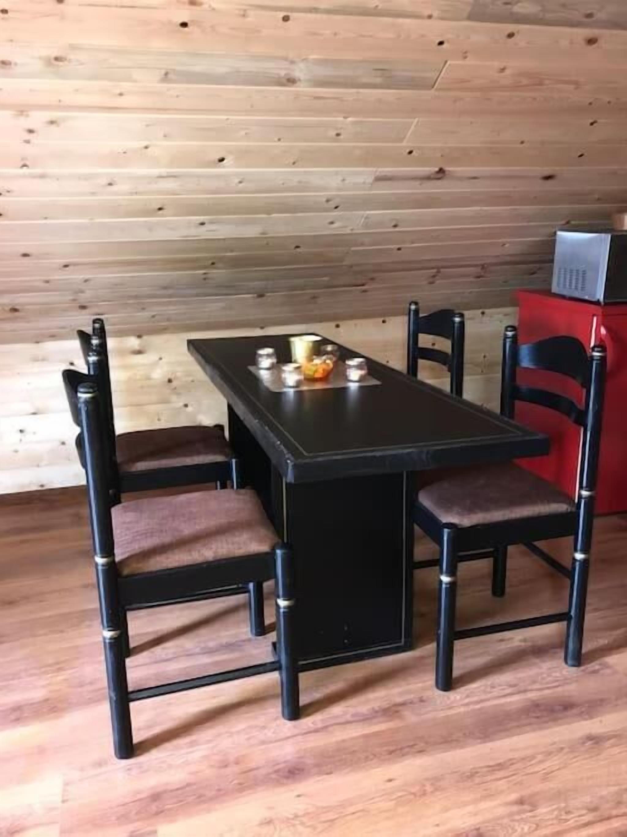 A dining table with four chairs, a small table lamp, and a red cabinet in a room with wooden walls.