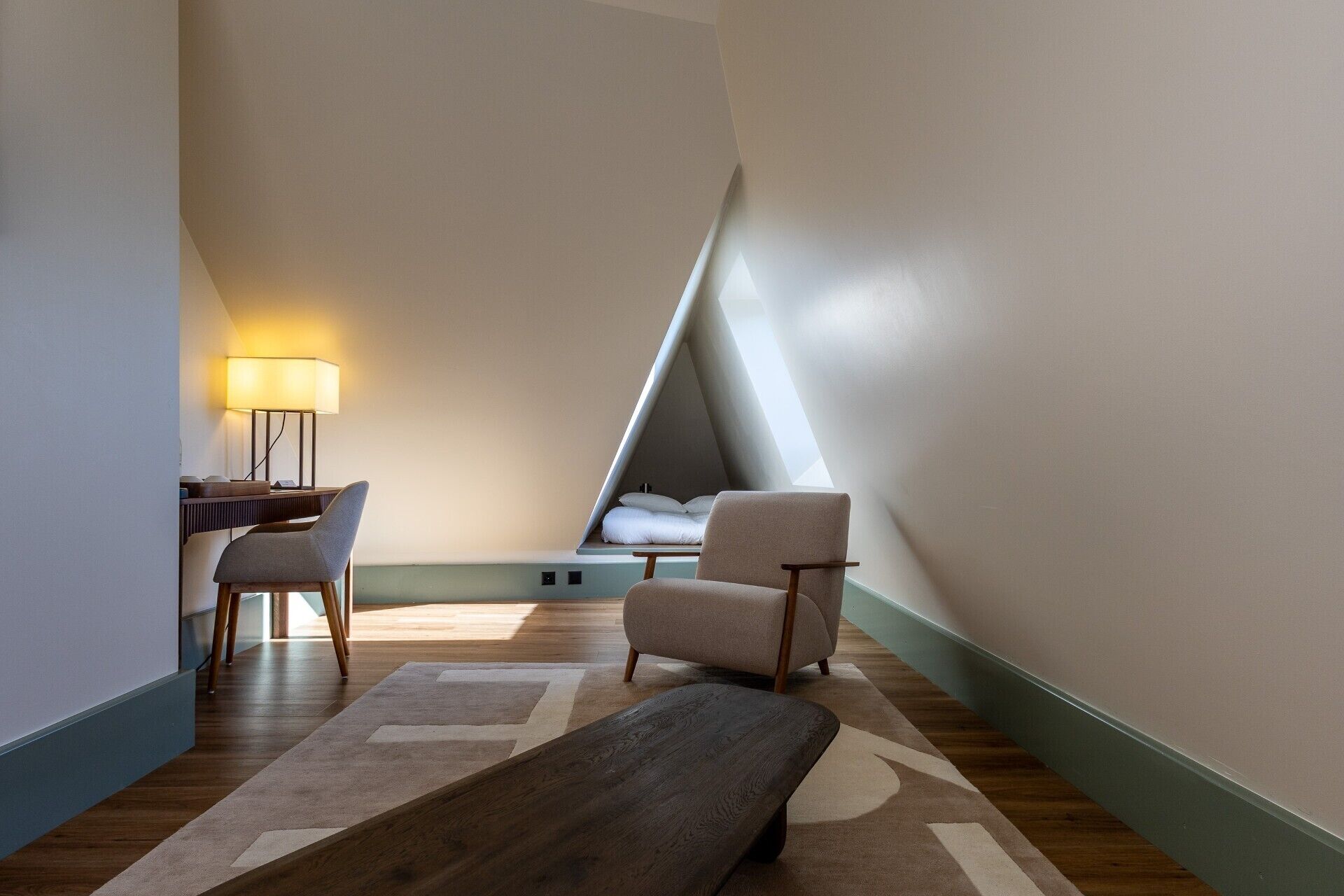 Un dormitorio estilo loft moderno con techo inclinado, un escritorio con lámpara, dos sillas y una cama.