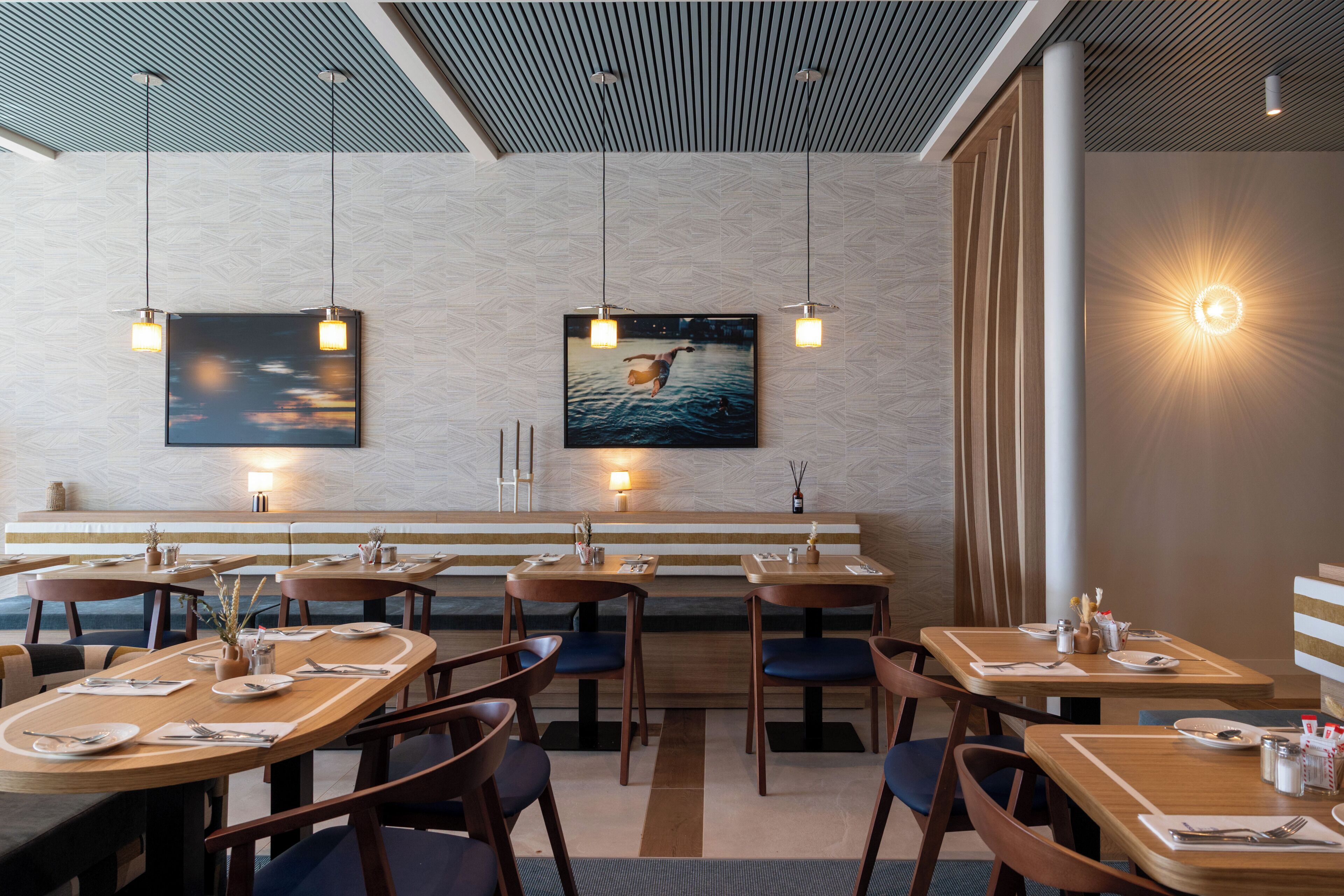 A restaurant with wooden tables and chairs, a bench seating area, and pendant lighting.