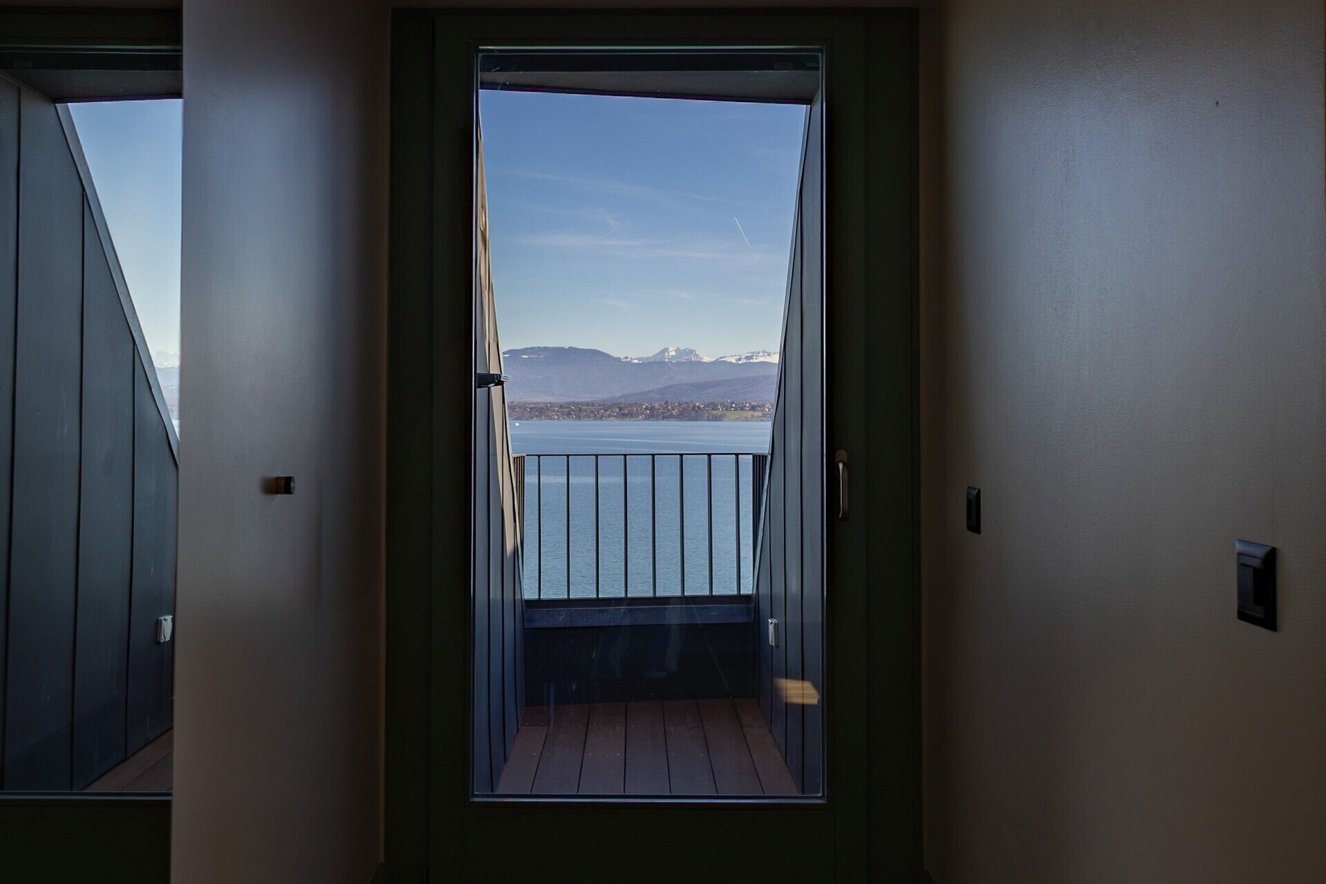 A view from a balcony with a metal railing, overlooking a body of water and distant mountains.