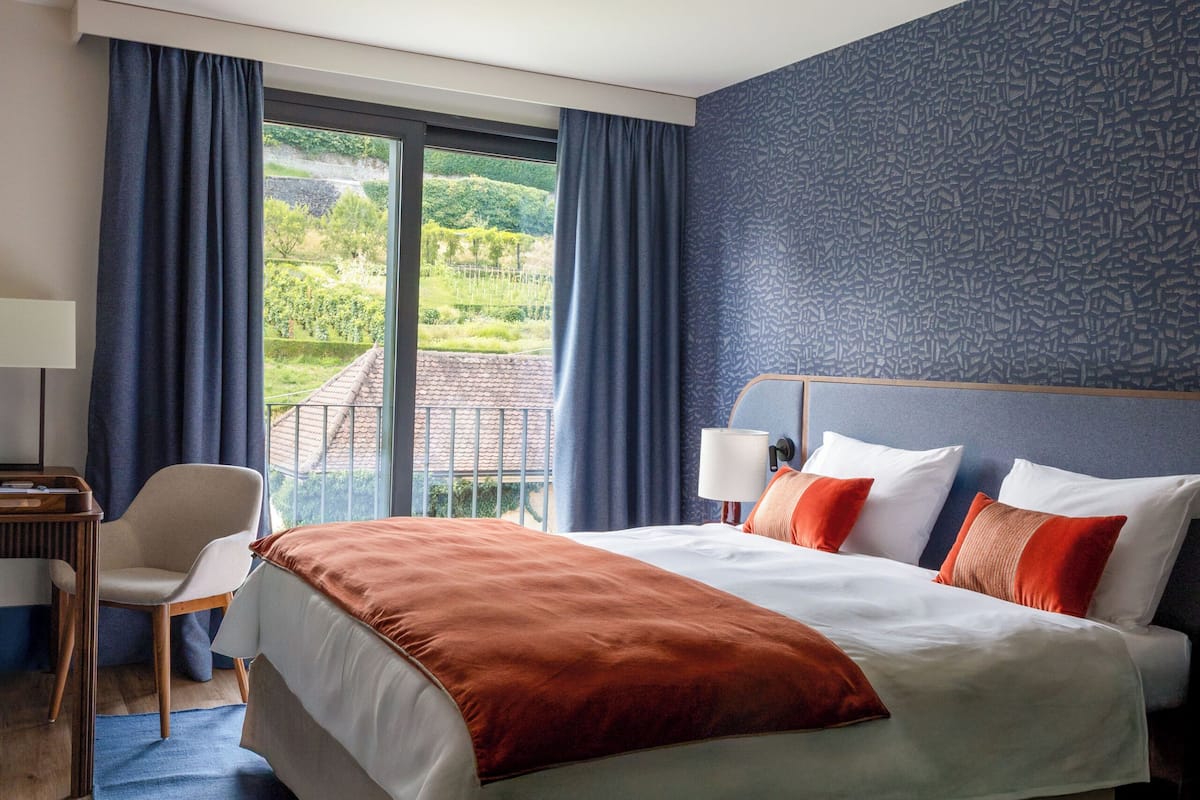 Une chambre d’hôtel avec un grand lit, une chaise, un bureau et une vue sur la verdure environnante.