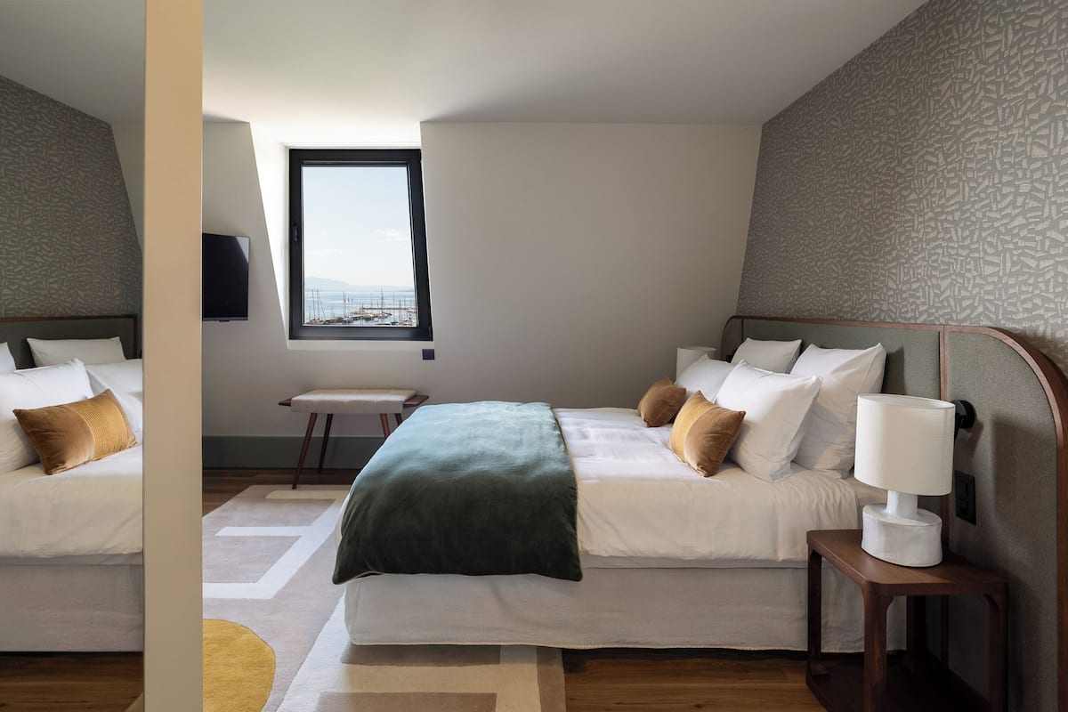Une chambre d’hôtel moderne avec deux lits, une grande fenêtre et un téléviseur fixé au mur.