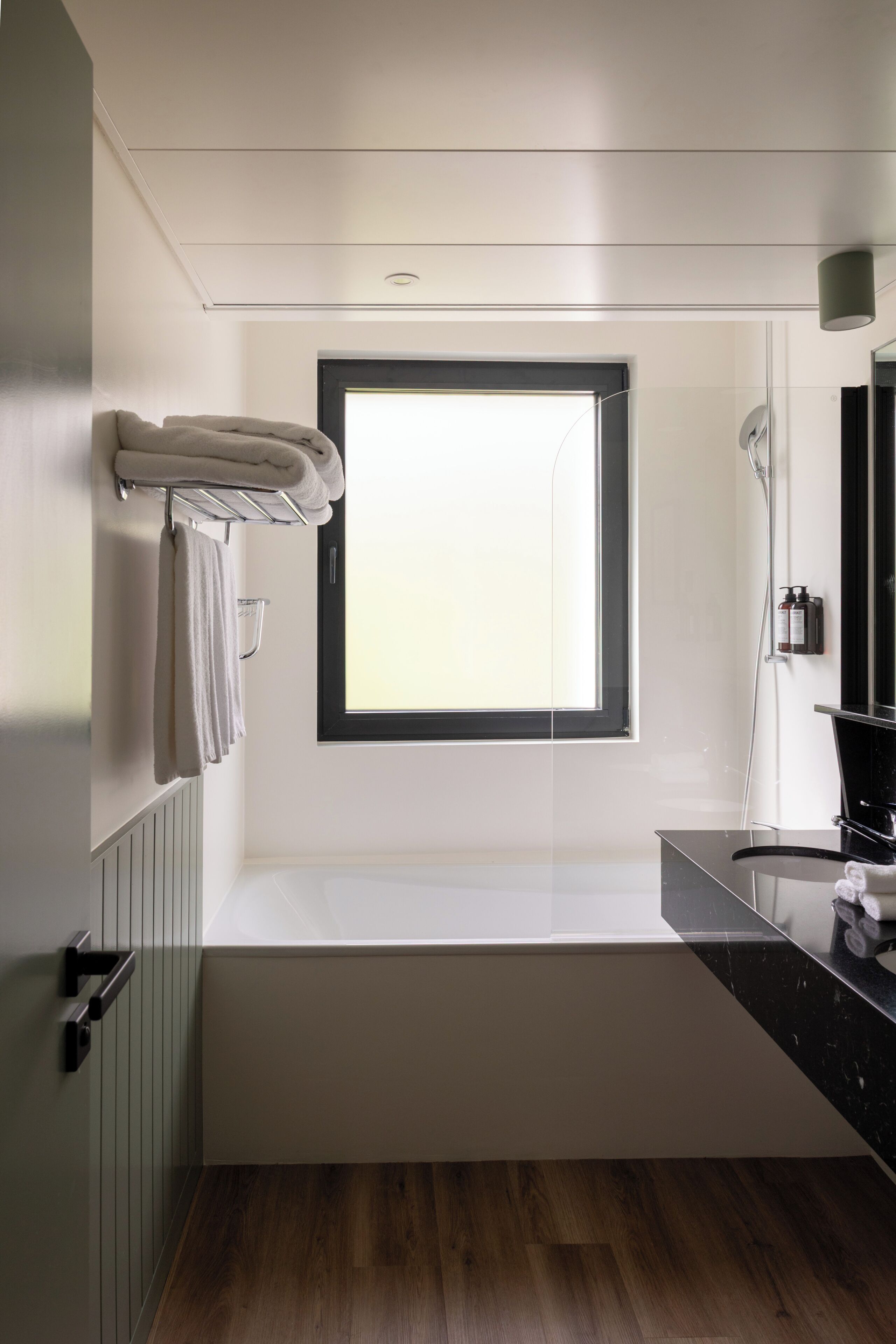 A modern bathroom with a large window, a bathtub, and a vanity with a mirror.