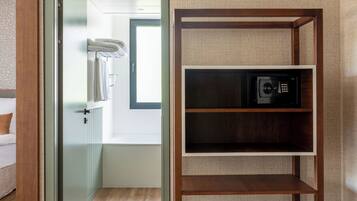 A hotel room with a wooden floor, a built-in shelf with a microwave, a towel rack, and a vent on the wall.