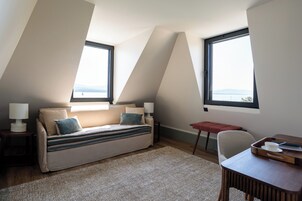 Un dormitorio tipo loft moderno con sofá cama, dos ventanas con vistas, una mesita y una silla.