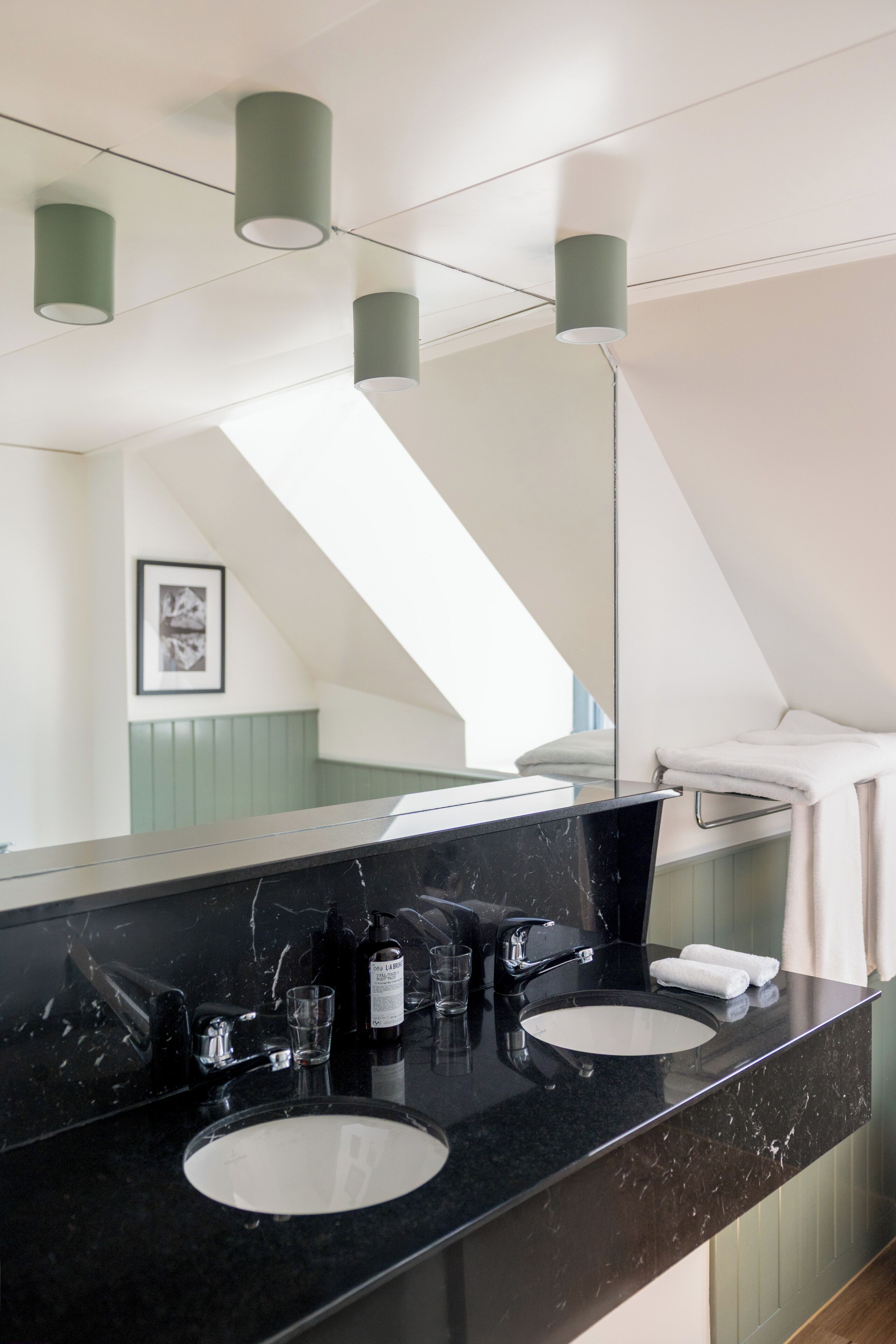 A modern bathroom with a black marble sink, two mirrors, and green pendant lights.
