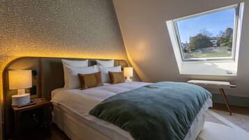 A bedroom with a sloped ceiling, a large window, a bed with white linens, and two bedside lamps.