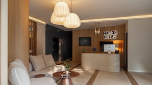 Un moderno vestíbulo de hotel con mostrador de recepción, un sofá, una mesa de centro y lámparas colgantes.