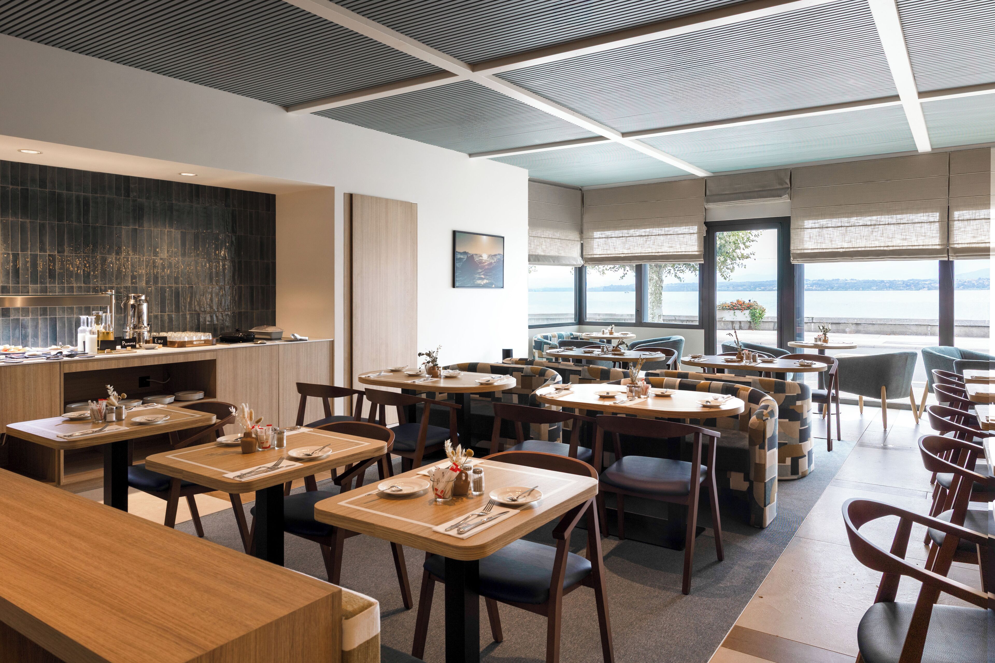 Un restaurant moderne doté de plusieurs espaces de restauration, d’une cuisine située à l’arrière et de grandes fenêtres offrant une vue sur l’eau.