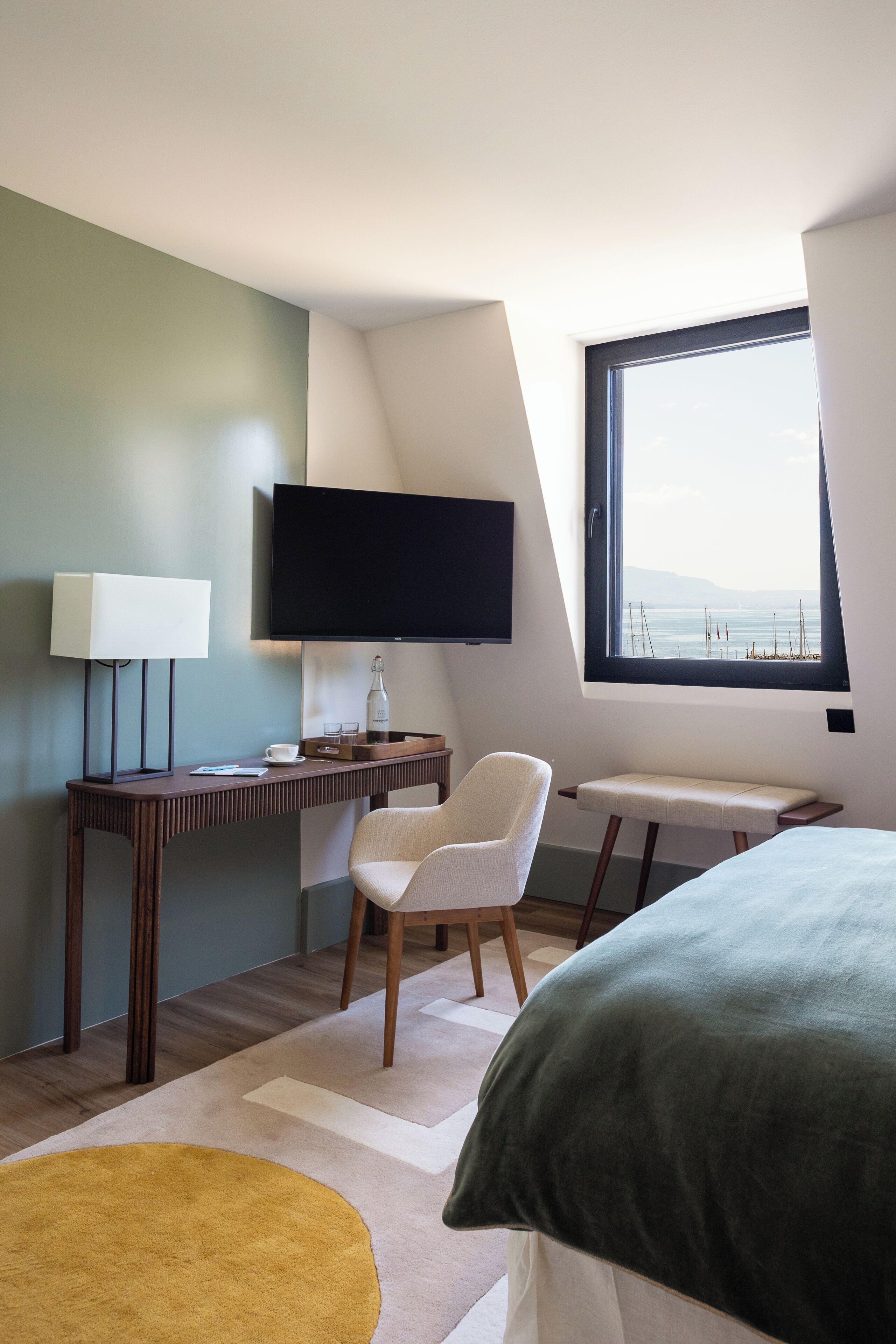 Quarto de hotel moderno com uma cama, uma mesa com cadeira, televisão e janela com vista para o mar.