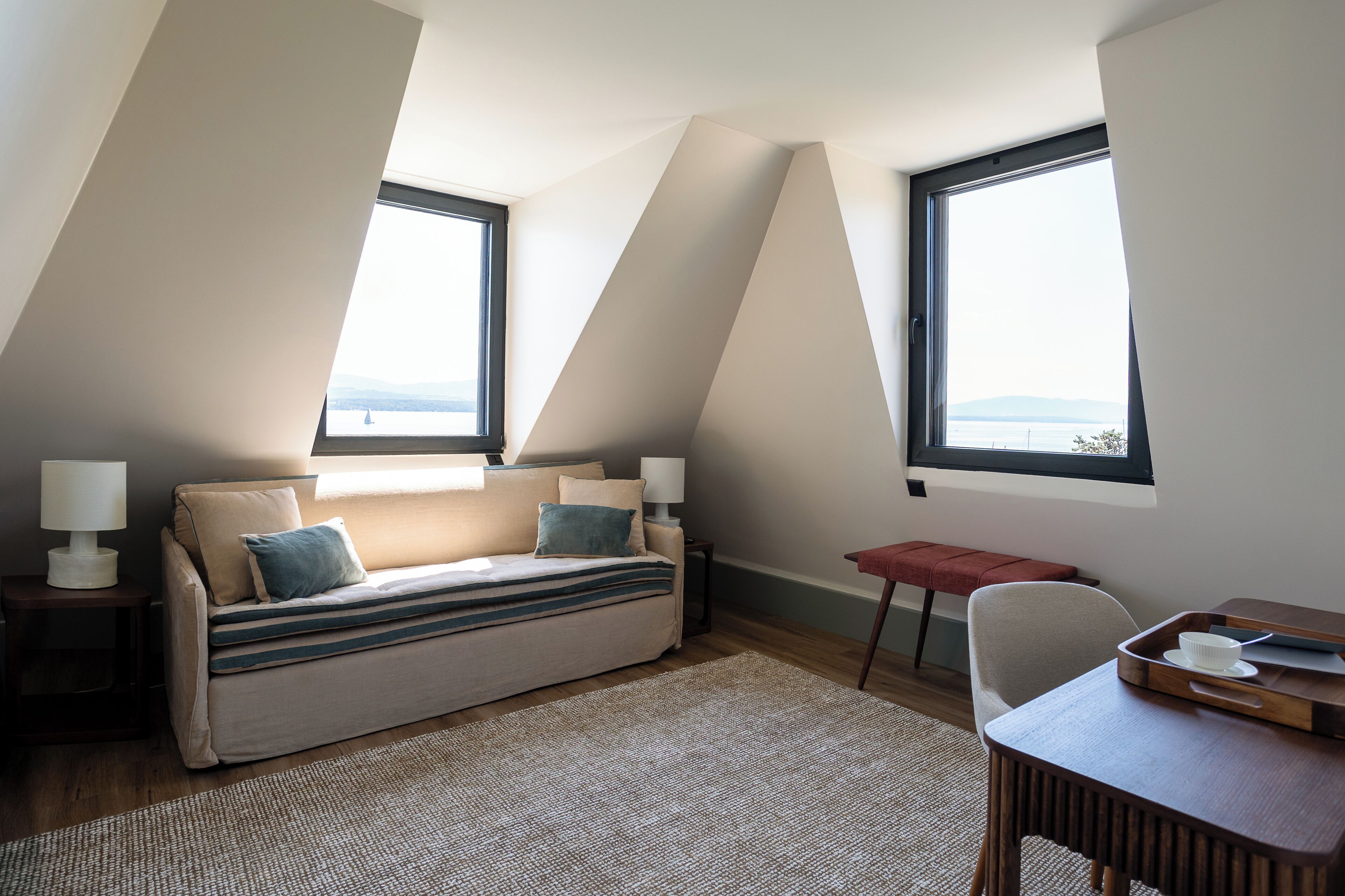 Un dormitorio tipo loft moderno con sofá cama, dos ventanas, una mesita y una silla.
