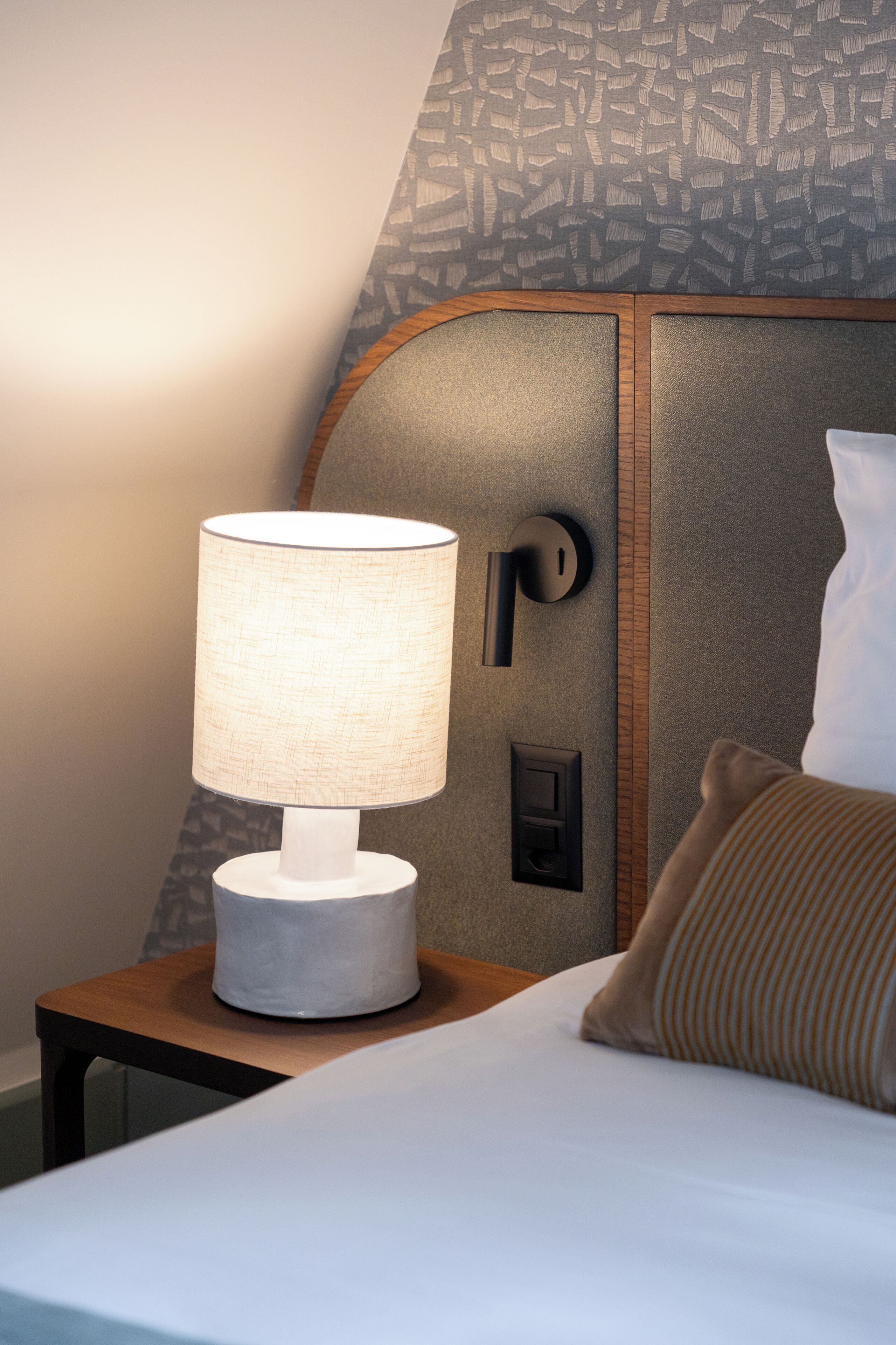 A neatly made bed with a white comforter, a bedside lamp, and a wooden nightstand.