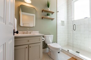 Bathroom features a vanity, toilet, shower, and wooden shelves.