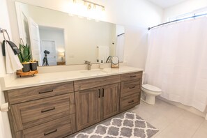 Ein modernes Badezimmer mit einem Doppelwaschbecken, Holzschränken, einem großen Spiegel und einer Duschvorhang.