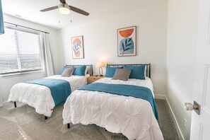 Ein Schlafzimmer mit zwei Betten, weißer Bettwäsche, Türkis-Akzenten und abstrakter Wandkunst.