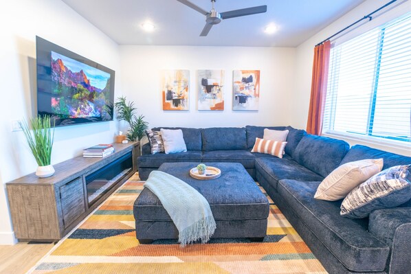 Ein modernes Wohnzimmer mit einem Ecksofa, einem flachbildfernseher an der Wand und einem Deckenventilator.
