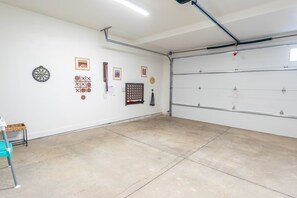Eine Garage mit Betonboden, einer Tür und verschiedenen Wanddekorationen, darunter eine Dartscheibe, gerahmte Bilder und ein Bulletin Board.