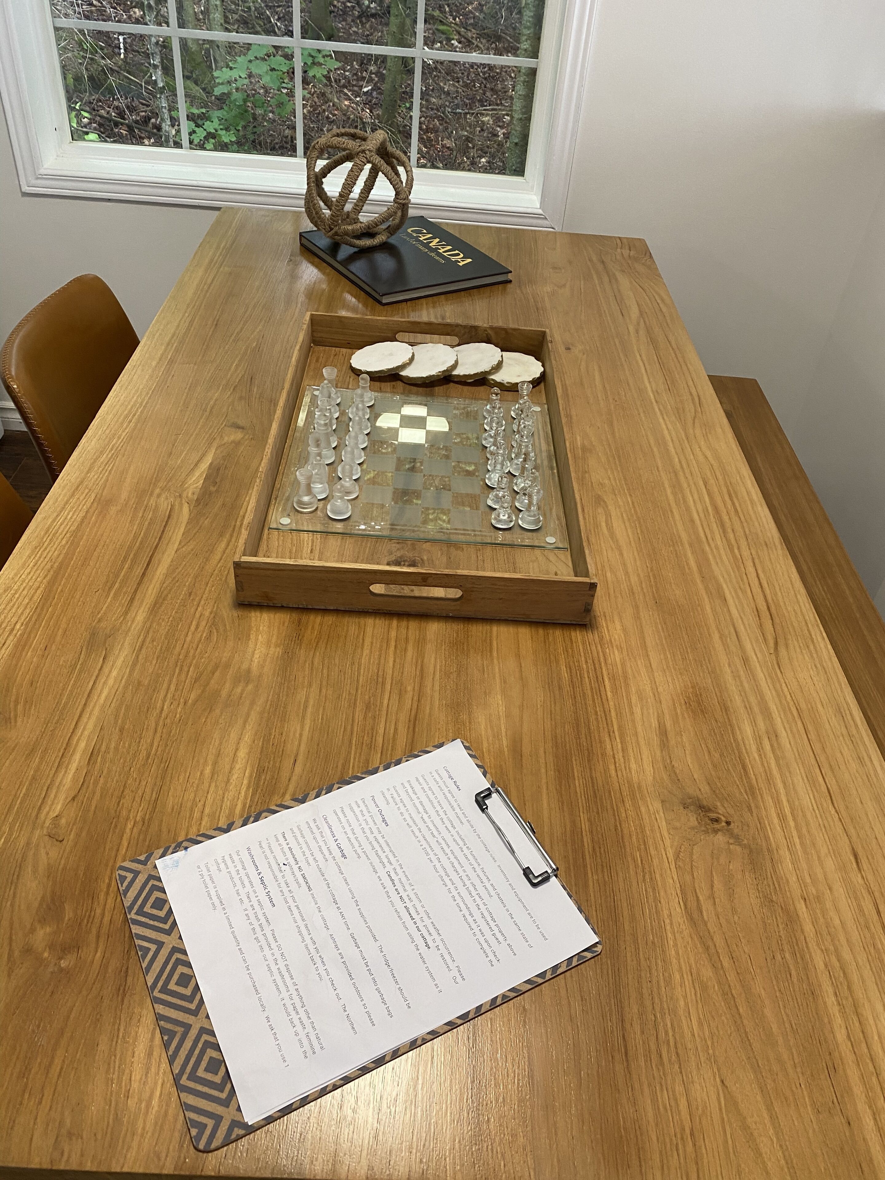 A wooden table with a chessboard, a book titled "CANADA," and a clipboard with papers.