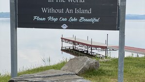 Willkommensschild für den See Bernard, den größten Süßwassersee der Welt ohne Insel, mit einem Steg und einer Rasenfläche im Hintergrund.