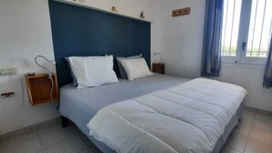 A bedroom with a bed, two bedside tables, a window with curtains, and a wall-mounted shelf.
