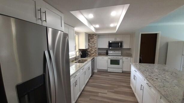 A modern kitchen with stainless steel appliances, white cabinets, and a herringbone wood backsplash. - 2 houses 5bed 4bath heated pool prime location (Valrico)